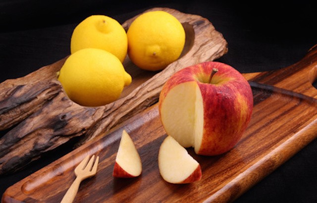 Cool organic fresh red apple on wooden tray with fork and cool lemons on classic tray isolated on black background